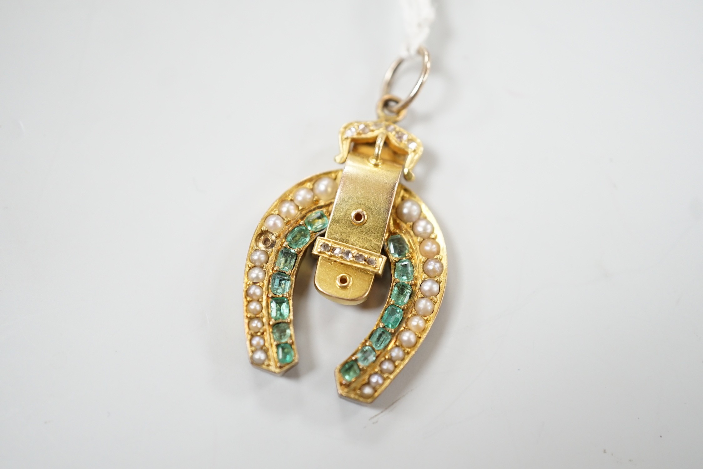 An early 20th century yellow metal, emerald, rose cut diamond and split pearl set horseshoe and buckle pendant, 33mm, gross weight 6 grams.